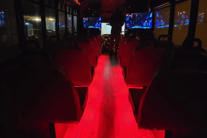 Bus interior with red floor lighting and screens showing images, silhouette of person near the front.