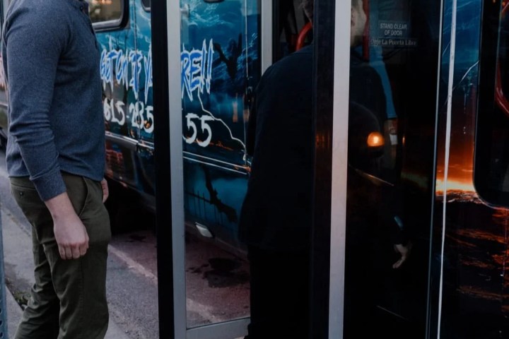 Two people boarding a bus with blue graphics in daytime.