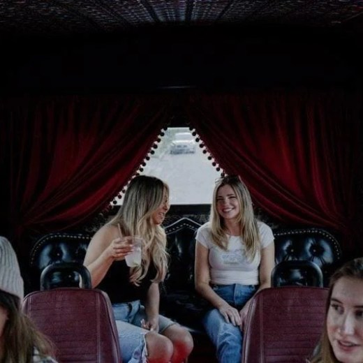 Group of women sitting and talking inside a vehicle with red curtains and seats.