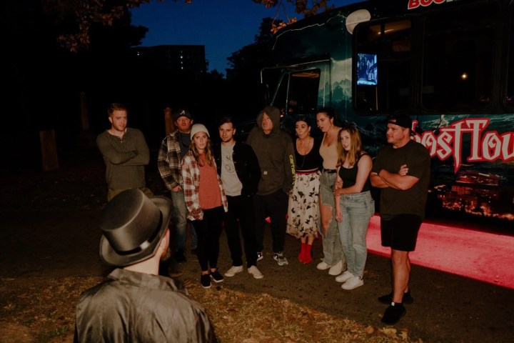 Group of people posing in front of a bus marked 'Ghost Tours' at night.