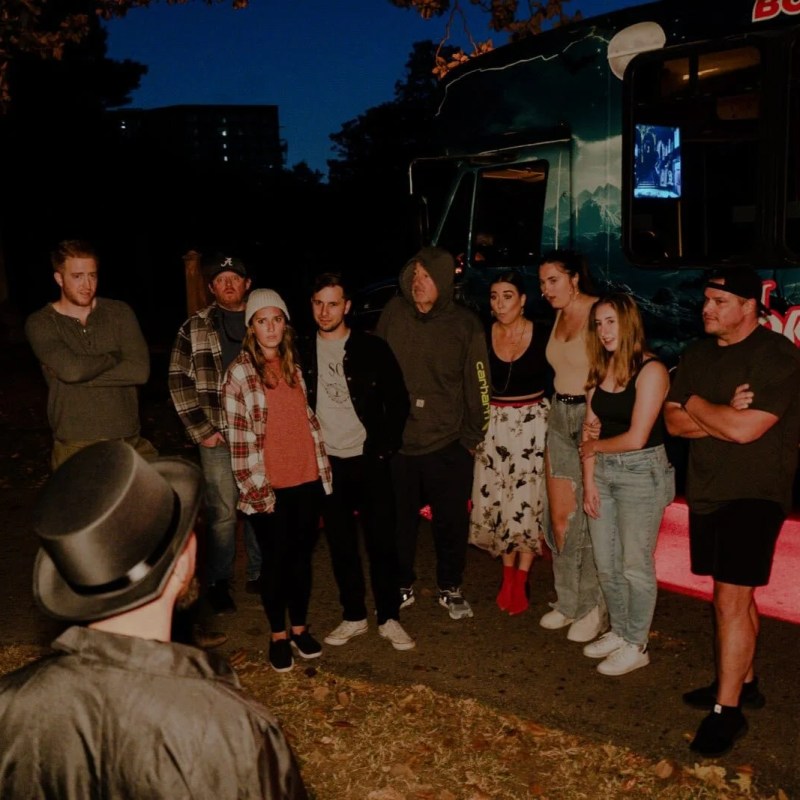 Group of people posing in front of a bus marked 'Ghost Tours' at night.