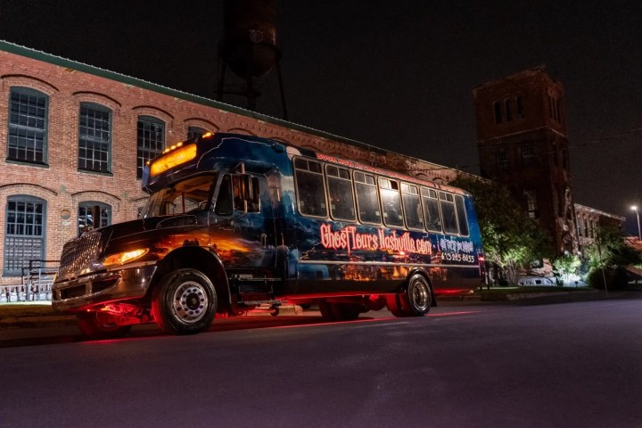 A ghost tour bus parked at night beside a brick building.