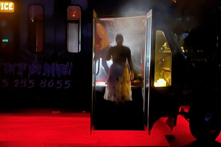Silhouette of person exiting bus with atmospheric lighting and red carpet.