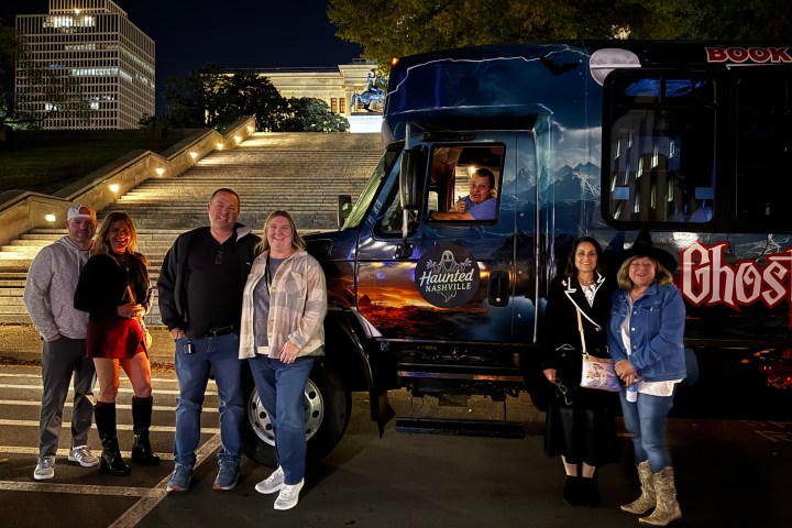 Group of people posing by a 'Haunted Nashville' tour bus at night.