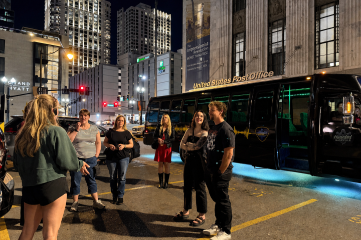 People standing near a bus labeled 'United States Post Office' on a city street at night.