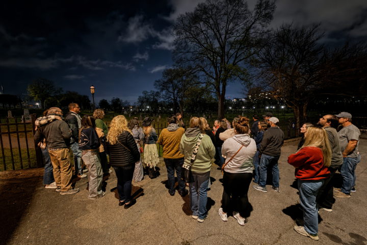 Group of people gathered under a cloudy night sky in a park.