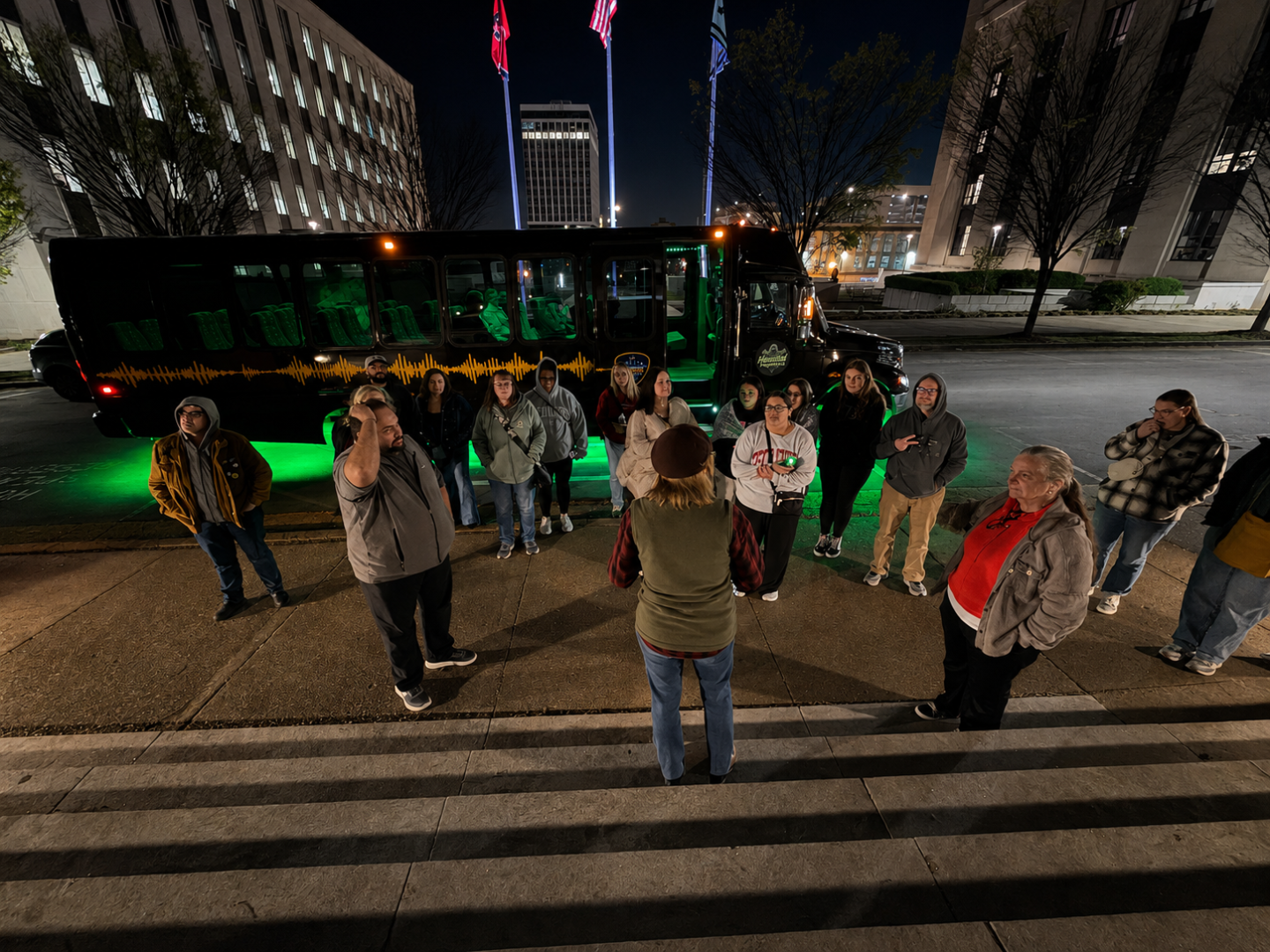 Group listening to a guide near a bus with green lights at night.