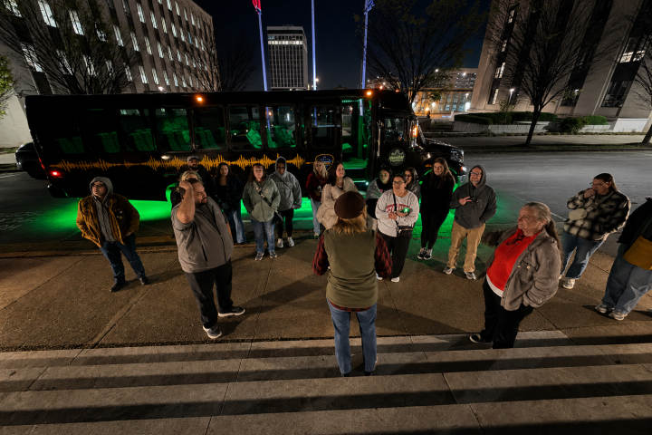 Group listening to a guide near a bus with green lights at night.