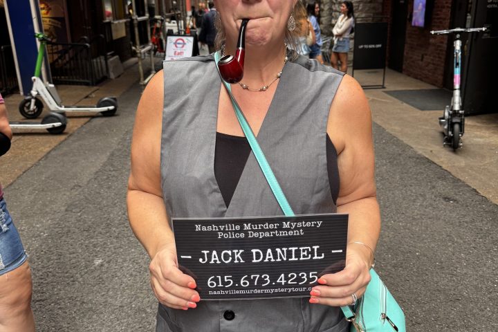 Nashville murder mystery pub crawl 22 Person in costume with pipe and mugshot sign on city street.