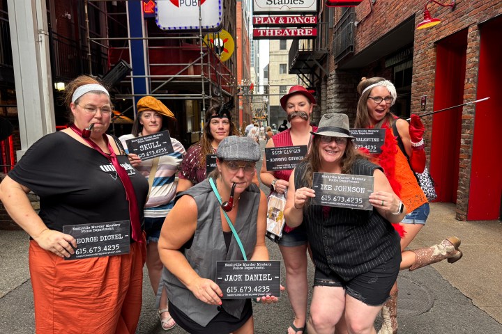 Nashville murder mystery pub crawl 22 Group dressed in vintage costumes holding props in an alley with neon signs.