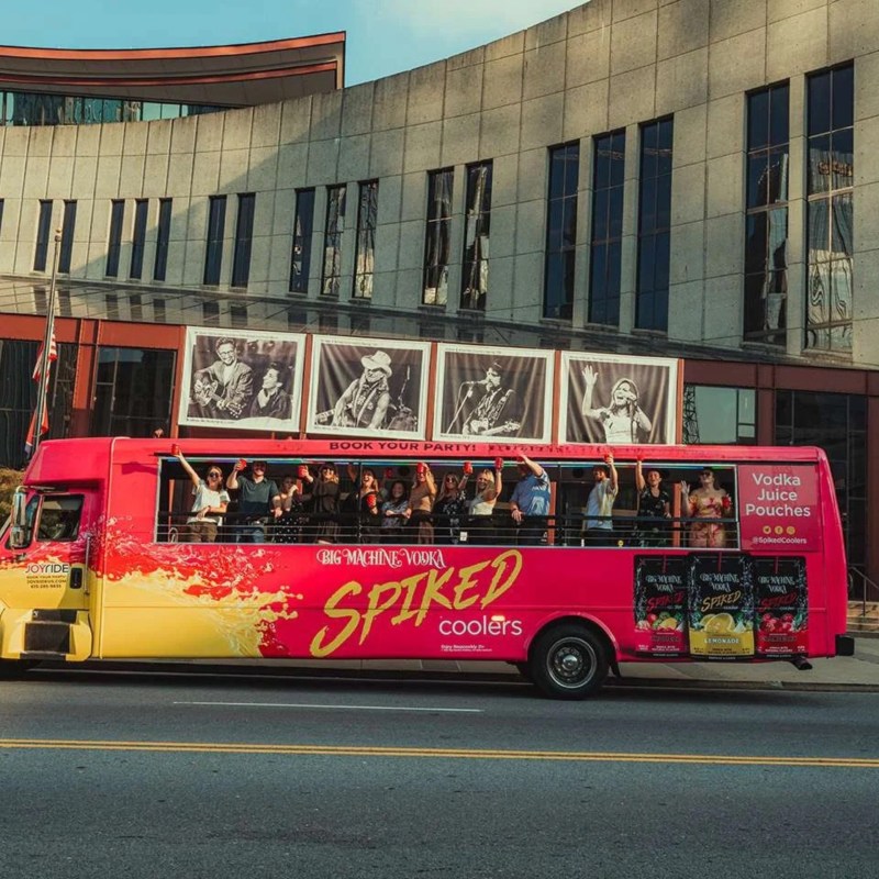 Red tour bus with people outside a modern building in daylight.