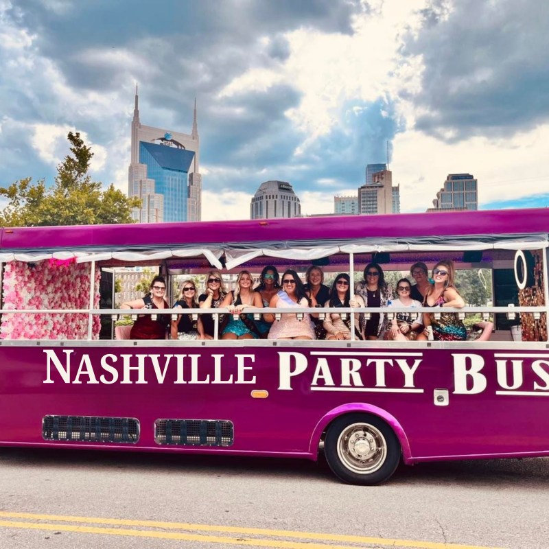 Pink party bus labeled 'Nashville Party Bus' with people inside, city skyline in the background.