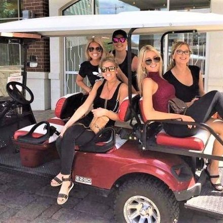 Five women sitting on and around a parked red golf cart, smiling at the camera.