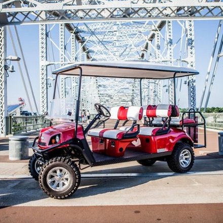 Red golf cart parked on a steel bridge on a sunny day.