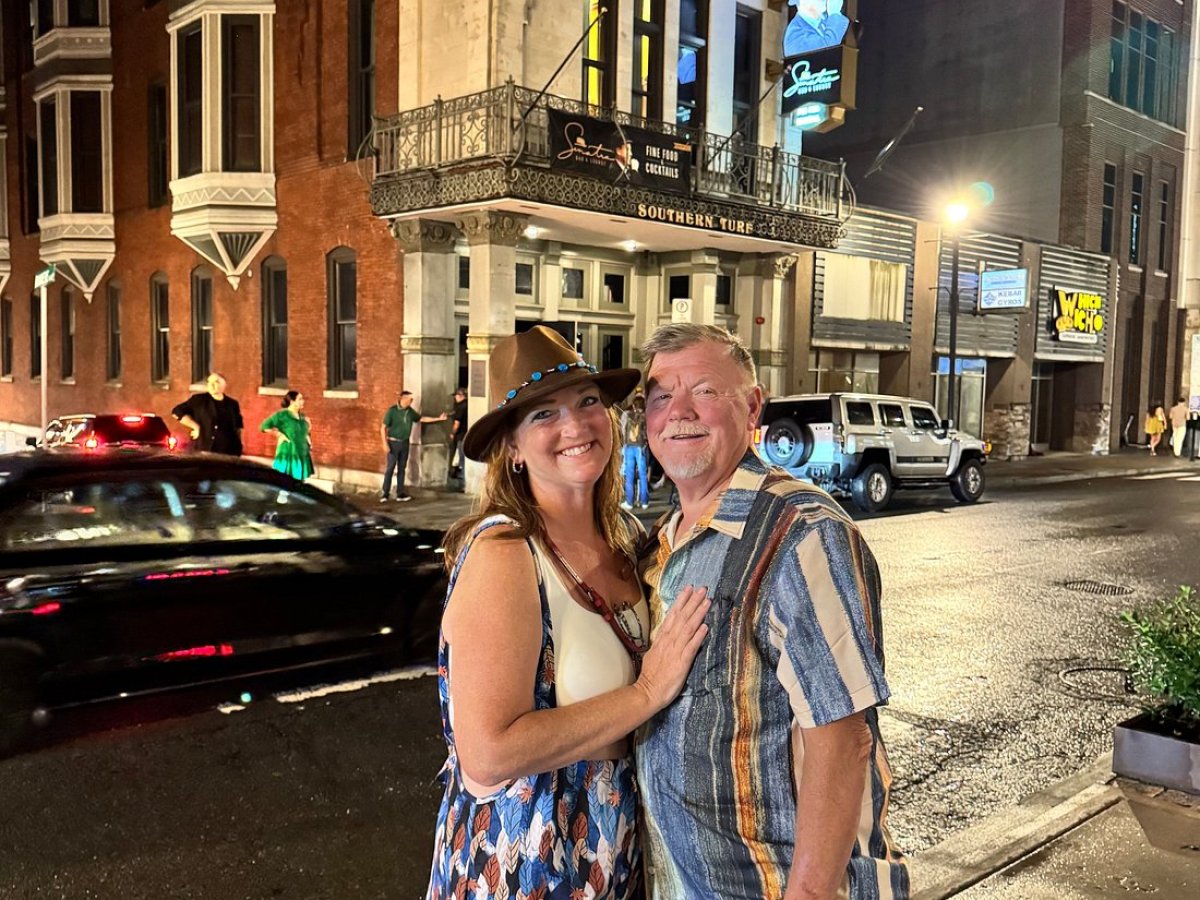 Smiling couple posing on a city street at night, in front of a lit building.