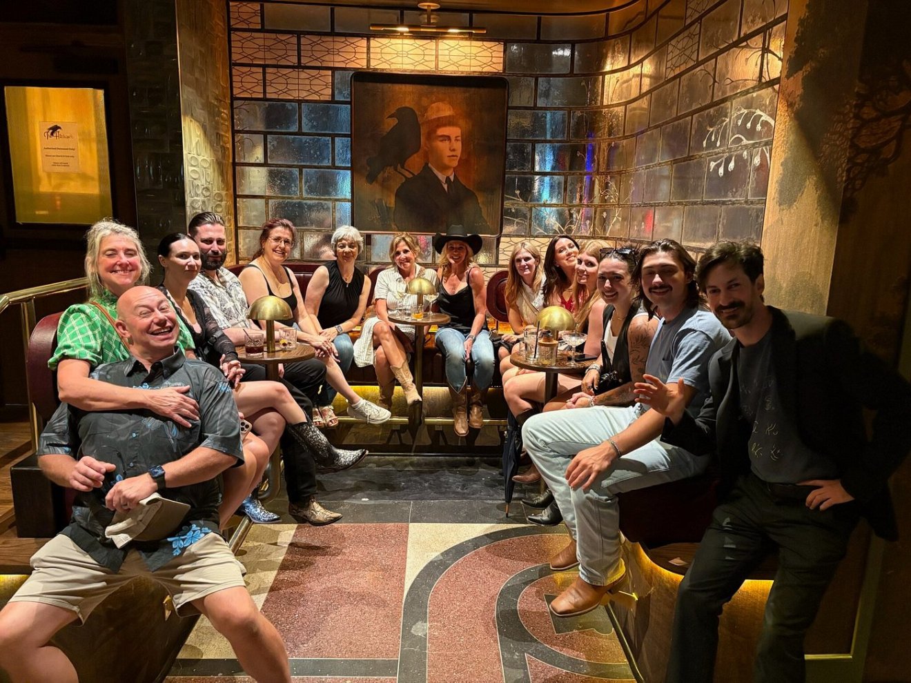 Group of people sitting in a room with a portrait on the wall and decorative lighting.