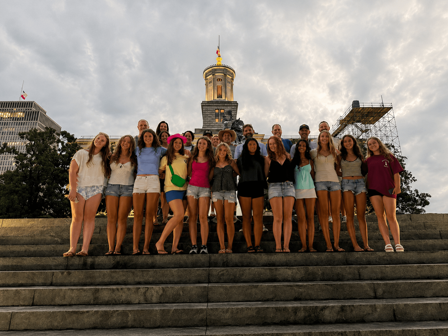 Group of people pose on steps with a building and cloudy sky at the tennessee state capitol on a haunted ghost bus tour in nashville in the background.